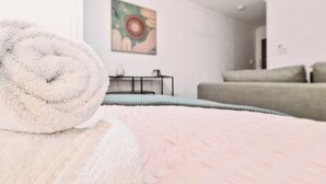 Un lit bien fait, avec une serviette blanche roulée, un canapé gris et un tableau accroché au mur.
