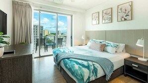 A bedroom with a bed, a desk, a chair, a balcony, and a city view.