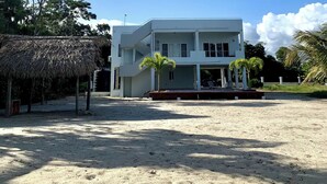 Ein zweistöckiges Gebäude mit flachem Dach und einem Balkon, umgeben von Sand und Palmen.