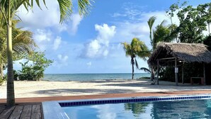 Blick auf einen Strand mit Pool, Palmen und einer Hütte mit Reetdach.