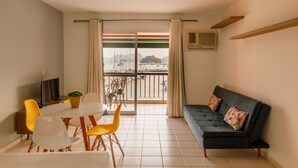 A living room with a sofa, a dining table with chairs, a TV, and a balcony with curtains. - Mares Suites by Angra Beach (Angra dos Reis)