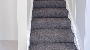 A staircase with dark carpeted steps and white handrails.
