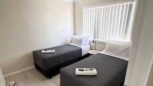 A small, clean room with two beds, a window with blinds, and a door with a key in the lock.
