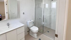 A modern bathroom with a marble vanity, a toilet, and a glass-enclosed shower.