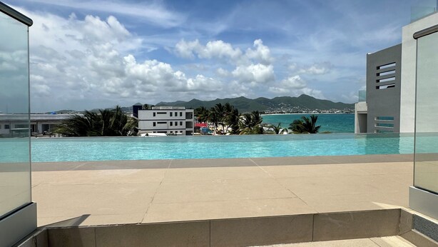 A modern pool area with clear blue water, a view of the sea, and distant mountains. - Beachfront Ultra Luxury - New Modern 2 Bed/2.5 Bath (Simpson Bay)