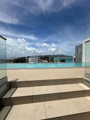 A modern pool area with clear blue water, a view of the sea, and distant mountains. - Beachfront Ultra Luxury - New Modern 2 Bed/2.5 Bath (Simpson Bay)