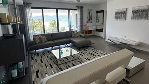 A modern living room with a large sofa, a coffee table, and a view of the outdoors. - Beachfront Ultra Luxury - New Modern 2 Bed/2.5 Bath (Simpson Bay)