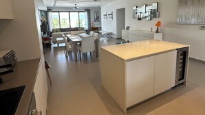 A modern kitchen with a central island, a dining area with a table and chairs, and a living space with a sofa and a TV. - Beachfront Ultra Luxury - New Modern 2 Bed/2.5 Bath (Simpson Bay)