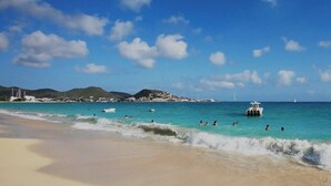 A beach with clear turquoise water, people swimming, and boats. - Beachfront Ultra Luxury - New Modern 2 Bed/2.5 Bath (Simpson Bay)