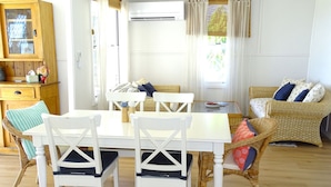A cozy living room with a dining table, white chairs, a wicker sofa, and a wooden cabinet.