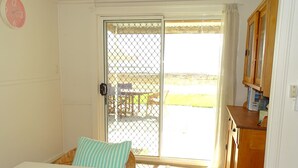 A room with a bed, a small table, a chair, a wooden cabinet, and a sliding glass door leading to an outdoor area.