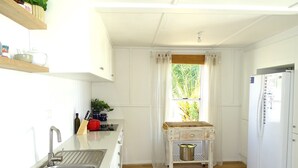 A compact kitchen with a sink, wooden countertop, white cabinets, a window with curtains, and a refrigerator.