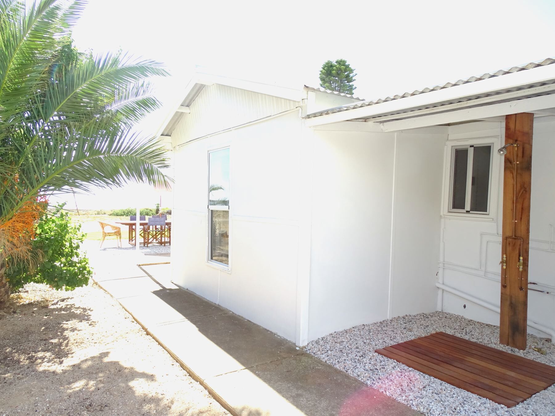 A white building with a wooden door, a window, and a small porch area with gravel and a wooden mat.