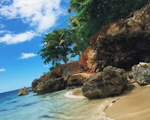 A beach with clear water, rocky formations, and palm trees.