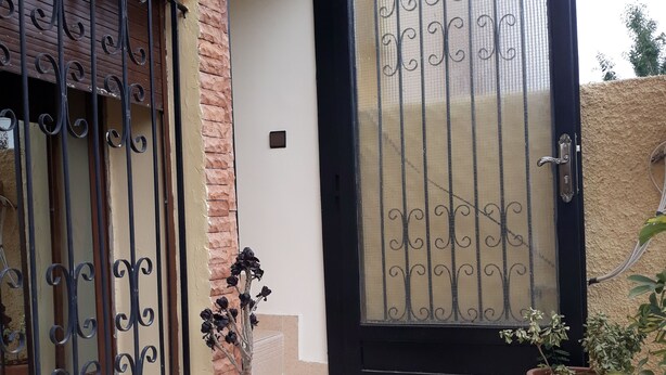 A building entrance with a black door, a window with decorative iron bars, and potted plants. - Cozy, Peaceful & Clean Studio Only 300 MAD (Ifrane)