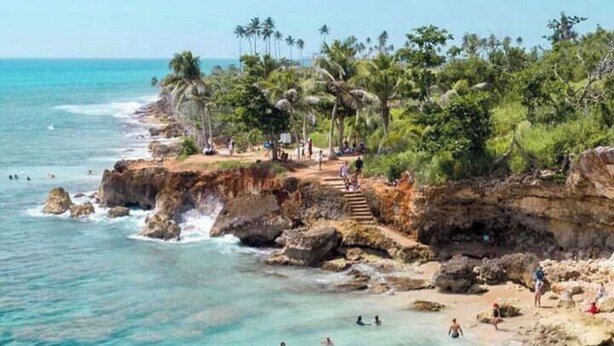 Una playa costera con aguas turquesas cristalinas, acantilados rocosos y palmeras.