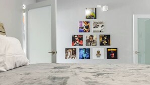 A bedroom with a bed, a marble floor, and a wall with framed posters. - Reggaeton Vibes! Puerto Rico's Legend Suite, Just 4 mins from Crash Boat Beach (Aguadilla)