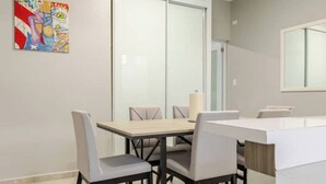 A modern dining area with a rectangular table and four chairs, a white countertop, and a glass partition. - Reggaeton Vibes! Puerto Rico's Legend Suite, Just 4 mins from Crash Boat Beach (Aguadilla)