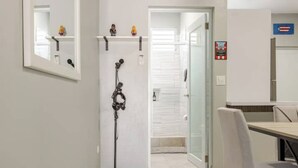 A hallway with a coat rack, a door leading to a bathroom, and a dining area with a table and chairs. - Reggaeton Vibes! Puerto Rico's Legend Suite, Just 4 mins from Crash Boat Beach (Aguadilla)