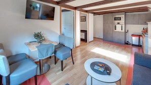A modern living room with a dining area, a kitchen with built-in appliances, and a TV mounted on the wall.