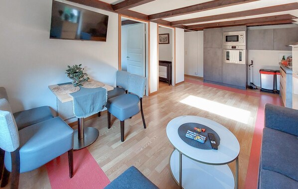 A modern living room with a dining area, a kitchen with built-in appliances, and a TV mounted on the wall.
