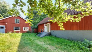 A red wooden building with a grey exterior, a small porch with steps, and a surrounding grassy area.
