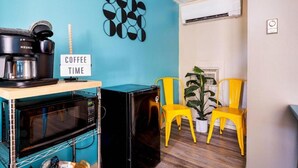 A kitchenette with a coffee maker, microwave, and a sign that says 'COFFEE TIME'. There are yellow chairs and a potted plant in the room.