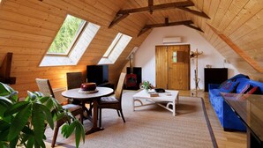 Un acogedor dormitorio en el ático con vigas de madera, una puerta de madera, un televisor, una chimenea, un sofá y una mesa de comedor.