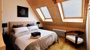 Un dormitorio con una cama grande, dos ventanas con persianas, techo de madera y un cuadro en la pared.