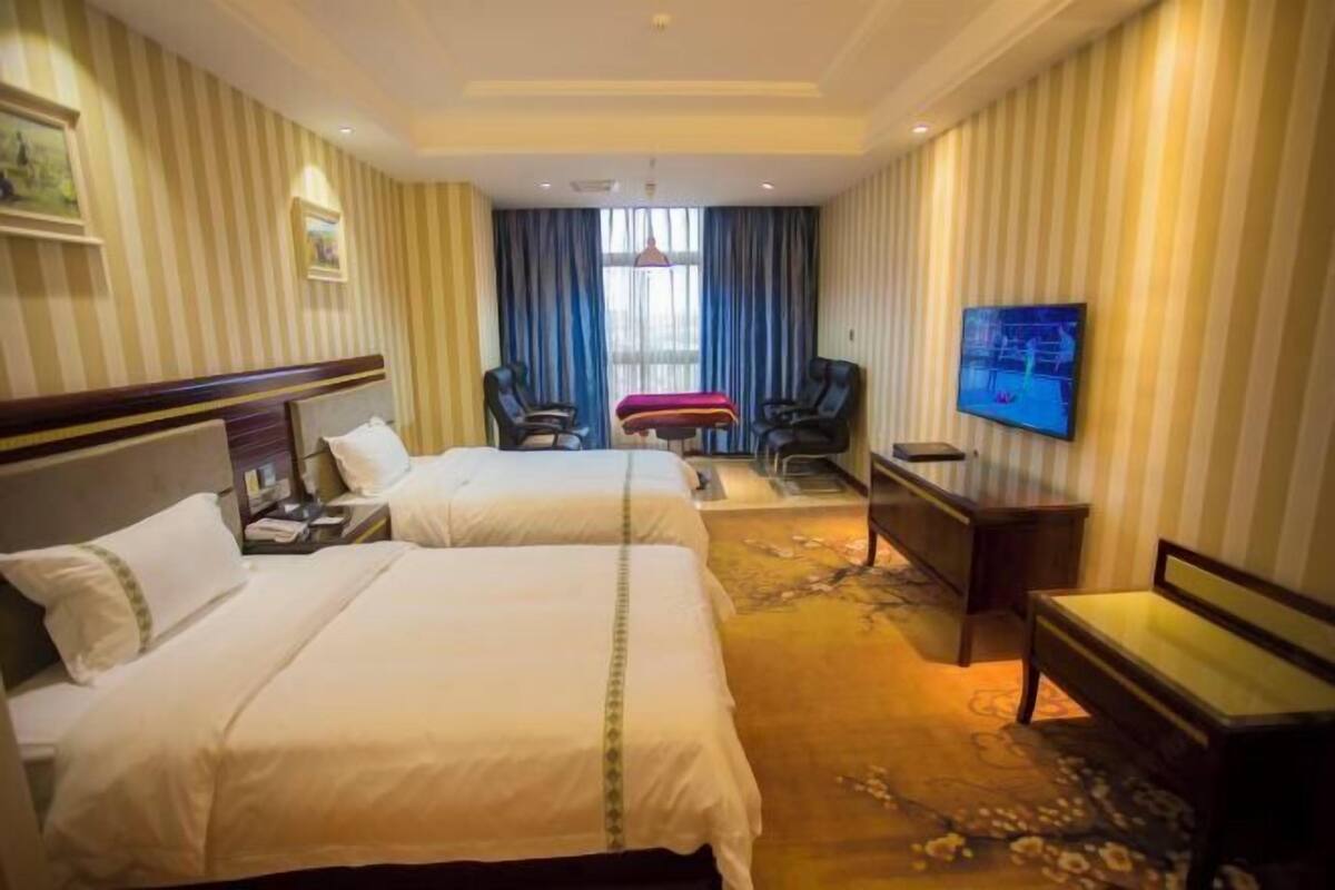 A hotel room with two beds, a desk, a chair, a television, and a window with curtains.