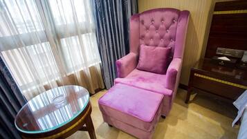 A room with a pink armchair, a glass table, and a wooden nightstand.