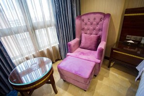 Una habitación con un sillón rosa, una mesita de vidrio y una mesita de noche de madera.