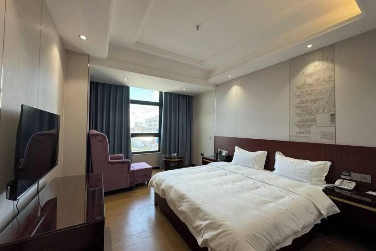 A hotel room with a large bed, a TV, a desk, and a chair.