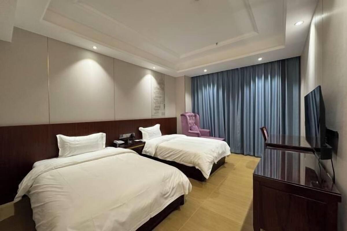 A hotel room with two beds, a TV, a desk, and a chair.