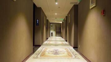 A hotel corridor with a patterned carpet, a fire alarm on the wall, and a door at the end.