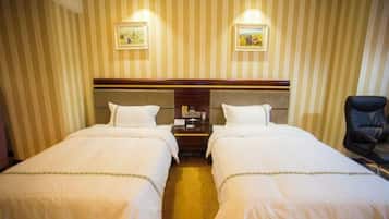 Una camera d'albergo con due letti singoli, una testiera in legno, un comodino con un telefono e una sedia.