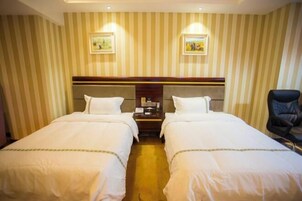 Habitación de hotel con dos camas individuales, cabecera de madera, mesita de noche con teléfono y una silla.