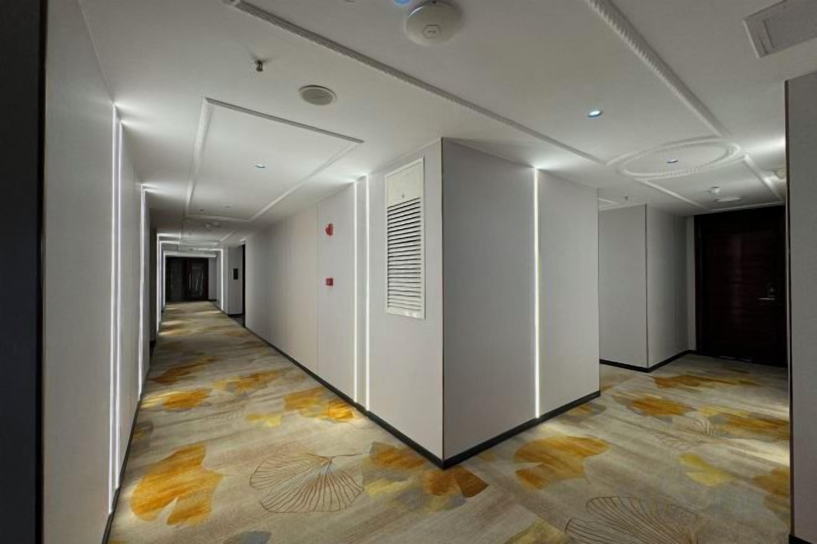 A hotel hallway with a patterned carpet, recessed lighting, and a modern design.