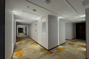 A hotel hallway with a patterned carpet, recessed lighting, and a modern design.