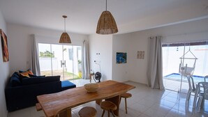 A modern living room with a wooden dining table, two hanging wicker lamps, a dark blue sofa, and a view of the outside through large windows. - Beachfront House with Sea Views, Pool and Independent Suites Pet Friendly (Touros)