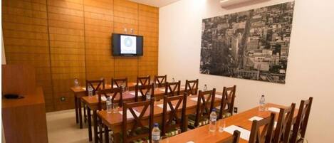 Un salón de conferencias con mesas y sillas de madera, un televisor de pantalla plana en la pared y un mural con vistas a la ciudad.