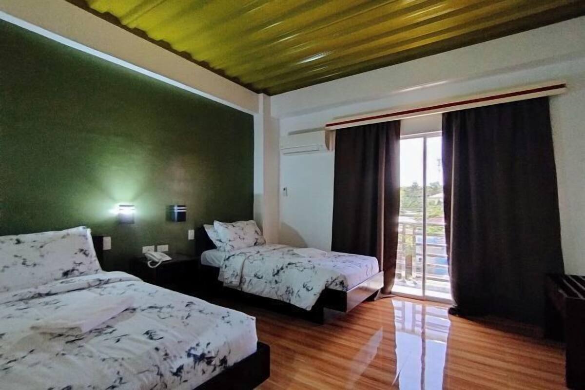 Ein Hotelzimmer mit zwei Betten, einem Balkon mit Vorhängen und einer grünen Wand.