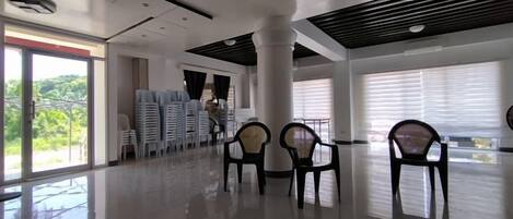 A spacious indoor area with a high ceiling, a large window with blinds, and several chairs arranged for seating.