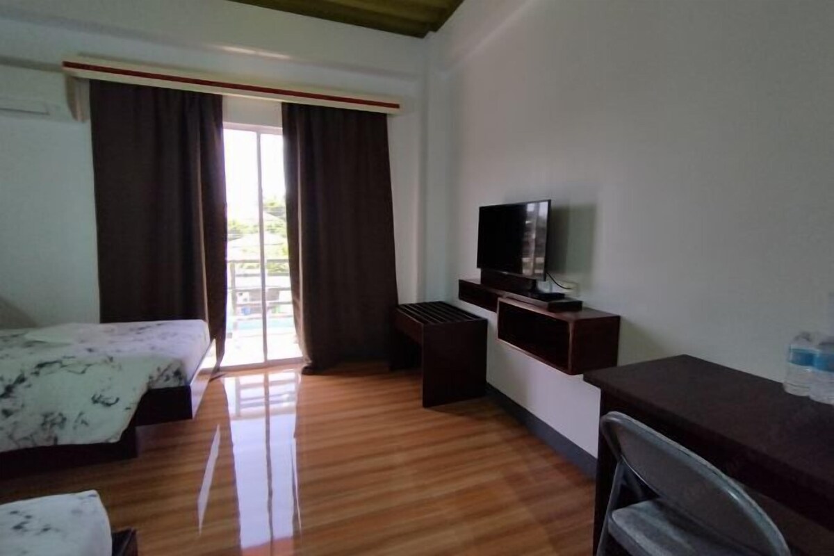 Habitación de hotel con cama, escritorio, televisor y ventana con cortinas.
