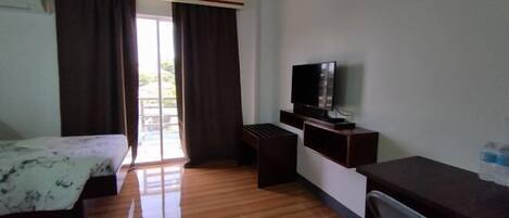 A hotel room with a bed, a desk, a television, and a window with curtains.