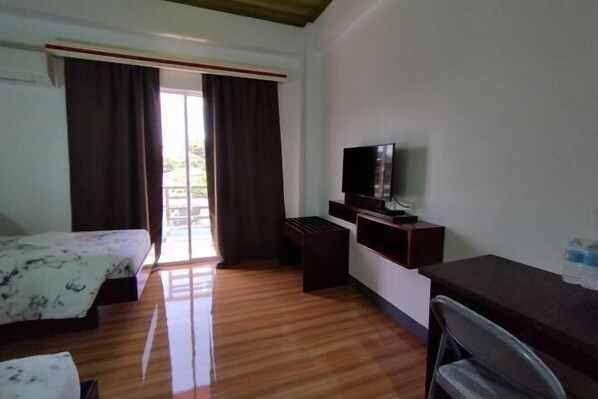 Habitación de hotel con cama, escritorio, televisor y ventana con cortinas.