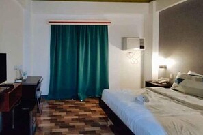Habitación de hotel con cama, escritorio, silla, televisión y ventana con cortinas.