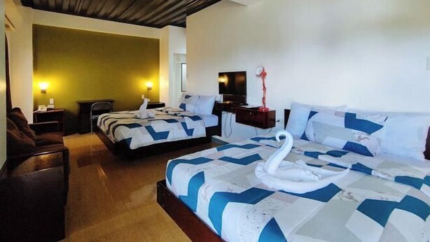 A hotel room with two beds, a sofa, a desk, and a TV.