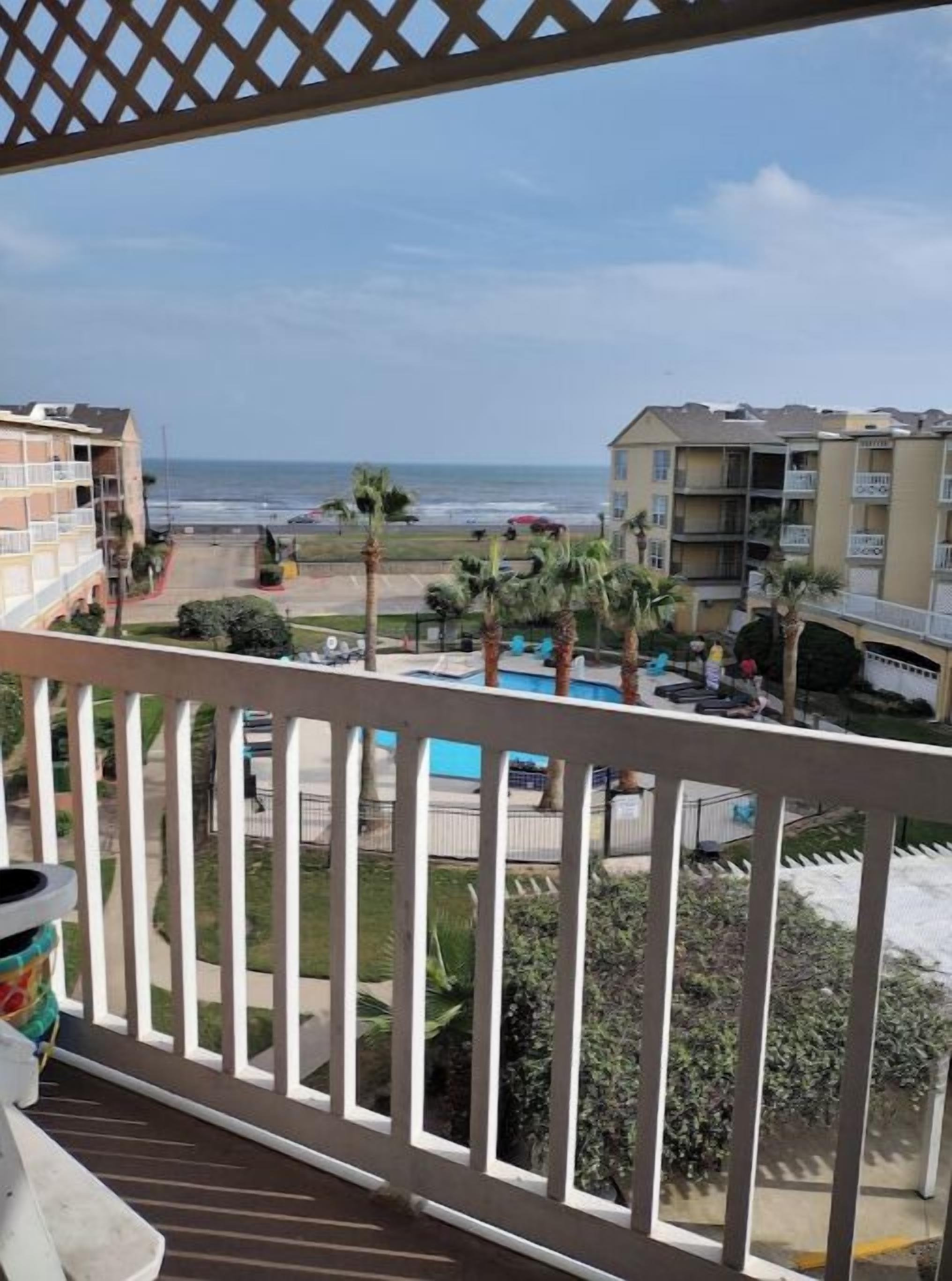 A balcony with a view of a swimming pool, palm trees, and a beach.