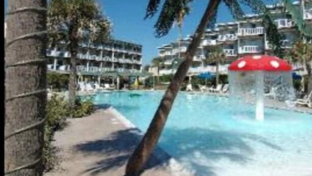 A pool area with palm trees and a building in the background. - Isle B Back Cozy 1-bedroom condo with WiFi, AC in amazing Galveston (Galveston)